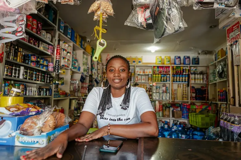 Comerciante sorridente no balcão de sua loja com prateleiras cheias